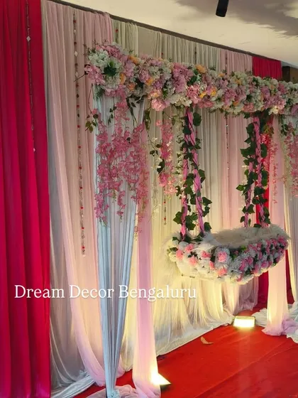 This angle shows the full stage with pink and white drapes. The hanging cradle and name reveal board create a complete and charming package for a baby girl's naming ceremony.