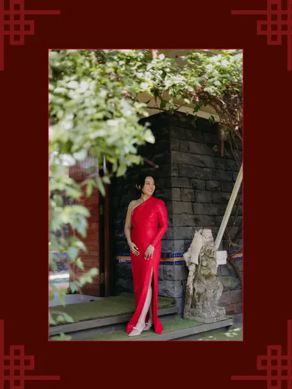 A full-length portrait of a woman in a striking one-shoulder red gown, posing confidently, framed by a traditional Chinese border.