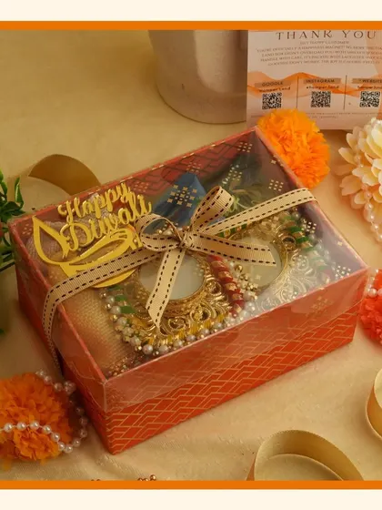 A transparent-lid box tied with a ribbon, featuring a "Happy Diwali" cutout and traditional diyas inside.