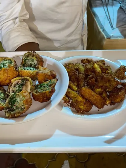 A tray of assorted fried starters, including bread rolls and corn patties, served with a dipping sauce.