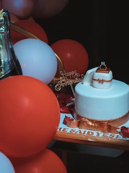 A different perspective of the "She Said Yes" proposal cake, showing it as part of a complete decorative setup with balloons and champagne.