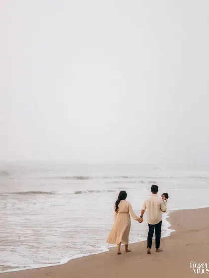 A family of three walks hand-in-hand along a misty shoreline. This wide shot creates a cinematic feel, emphasizing their journey together against the vastness of the ocean.