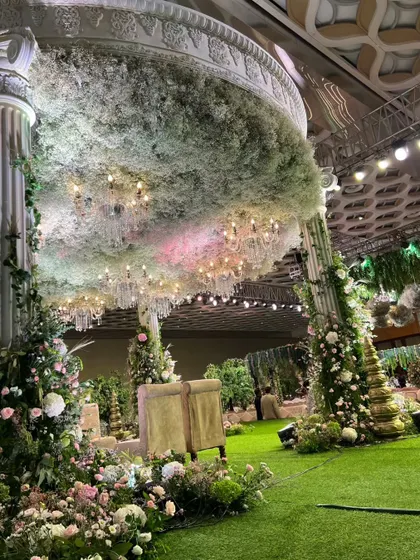 A view of the mandap from the side, showing the lush green carpet, the floral-wrapped pillars, and the magnificent baby's breath ceiling.