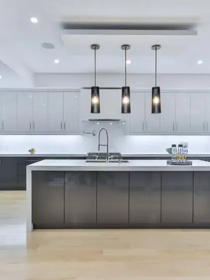 A luxurious and expansive kitchen with a large central island perfect for entertaining. The design features sleek, high-gloss grey cabinetry, dual wall ovens, and sophisticated pendant lighting.