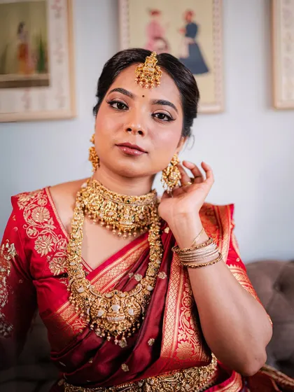 A close-up of a bride in a red silk saree, her look elevated by an intricate temple jewellery set. The craftsmanship is designed to make you feel like a goddess.