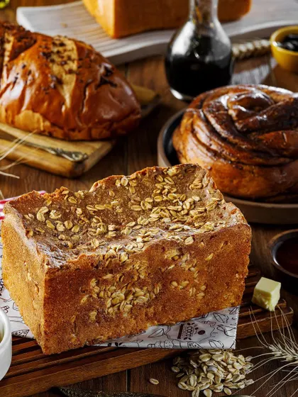 A beautiful arrangement of various freshly baked breads and pastries. This shot showcases a variety of textures, from an oat-topped loaf to a sweet cinnamon roll, creating a visual ode to the art of baking.
