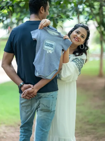 A cute announcement photo where the mom-to-be holds a "Future Gamer" onesie, with her partner's back to the camera.