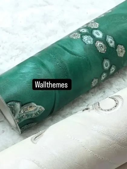 A close-up of two wallpaper rolls, one in a rich emerald green and one in off-white, with a textured damask pattern.
