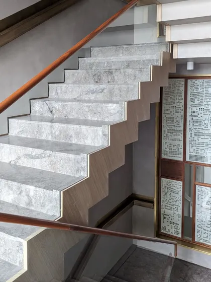 A view of the marble staircase alongside a detailed Sanjhi screen. The geometric precision of the traditional craft complements the clean lines of the modern staircase, creating a dialogue between two different design languages.