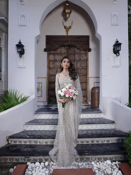 A serene and elegant portrait. The model is styled in a beautiful silver-grey saree by Anjalee and Arjun Kapoor, holding a bouquet. This look is perfect for a sophisticated reception or a Christian bride.