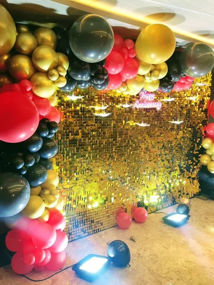 A bold and dramatic party backdrop combining a gold sequin wall with a balloon arrangement in red, black, and gold.