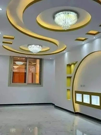 I specialize in creating complex, curved designs with gypsum. This living room features a flowing false ceiling with integrated chandeliers and cove lighting, which continues down into a custom-built wall unit with illuminated display niches.