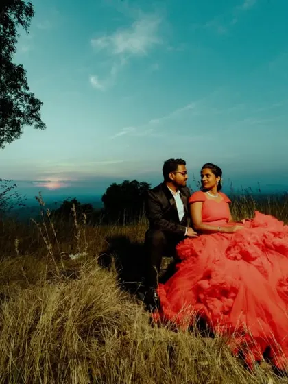 A beautiful pre-wedding portrait at dusk. The vibrant red of the bride's dress stands out against the serene landscape.