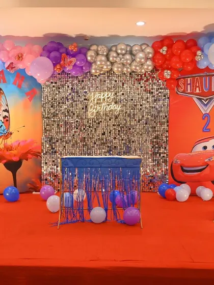 A unique twins' birthday party combining a butterfly theme and a Cars theme. The stage features a central shimmer wall and two distinct themed backdrops.