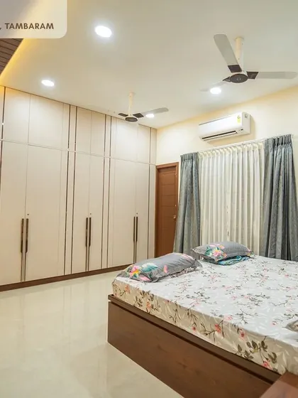 This spacious bedroom in the Tambaram villa includes a full wall of off-white wardrobes with long handles, providing ample storage while maintaining a clean, minimalist look.