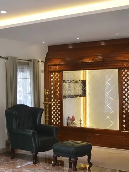 This classic living area features a beautifully crafted, large-scale wooden pooja unit with intricate jaali work. The space is furnished with a vintage-style leather armchair and a grandfather clock, creating a timeless and elegant corner.