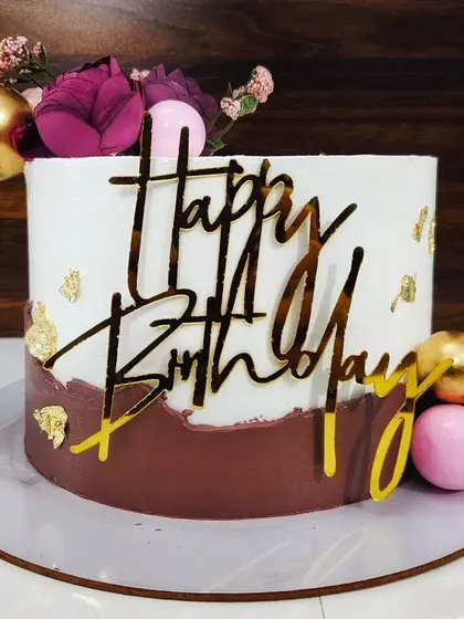 A feminine cake in brown and white with gold accents. This vanilla and strawberry cake is adorned with flowers and chocolate spheres for an elegant look.