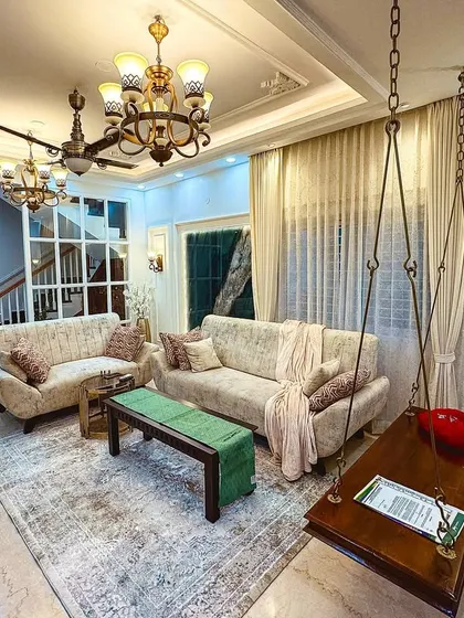 A living room that perfectly fuses Indian heritage with European classicism, featuring a traditional wooden jhula (swing) and elegant wall mouldings.
