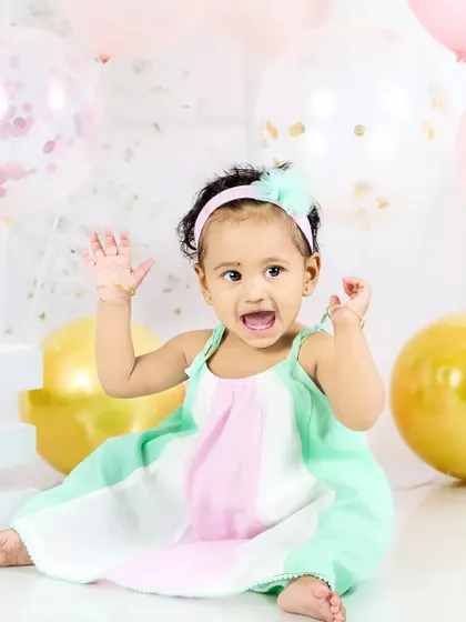 A baby girl throws her hands up in excitement during her first birthday photoshoot. Her joyful expression is priceless.