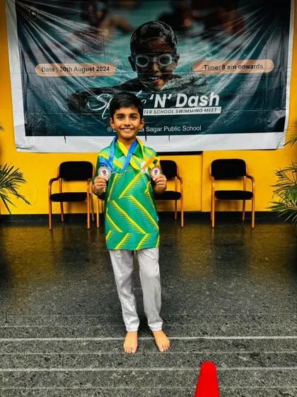 Aryan Sagar Chandra stands in front of the competition banner, proudly showing his medals from the Splash N' Dash event.