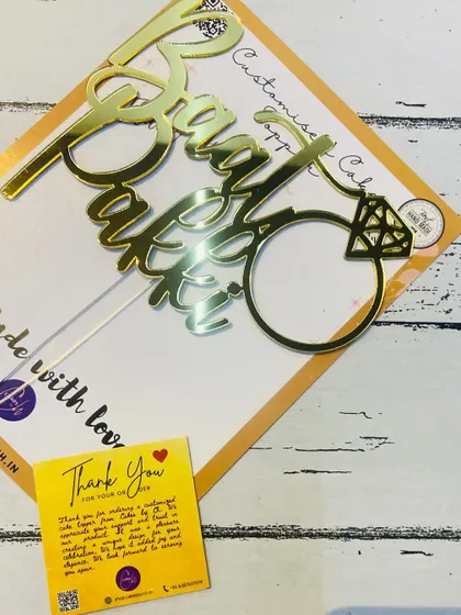 A close-up of the "Baat Pakki" topper, showing the detail of the ring and the script.