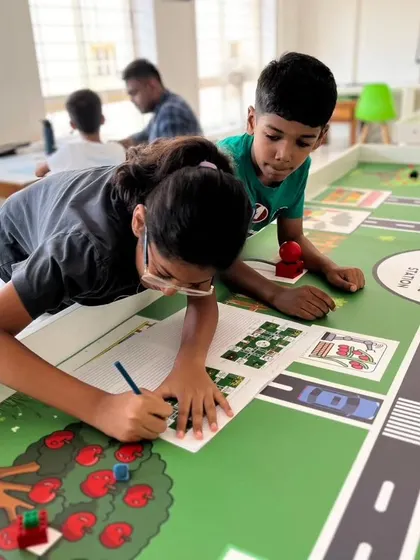 Two students collaborate closely, with one sketching out a plan while the other observes the challenge mat. This shows the blend of design, strategy, and teamwork in our IRO preparations.