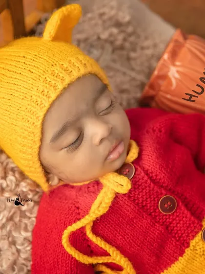 A close up of a newborn's peaceful face, dressed in a hand knitted Winnie the Pooh outfit. I pay close attention to details like the soft 'hunny' pot prop.
