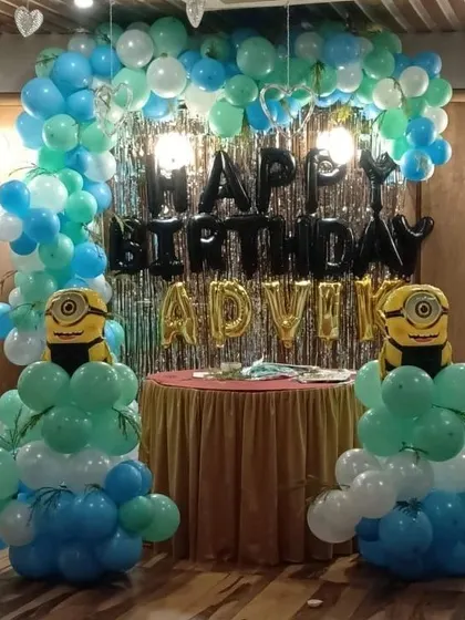 A fun Minions-themed birthday party. This setup includes a balloon arch in shades of blue and green, with two Minion balloon pillars guarding the cake table.