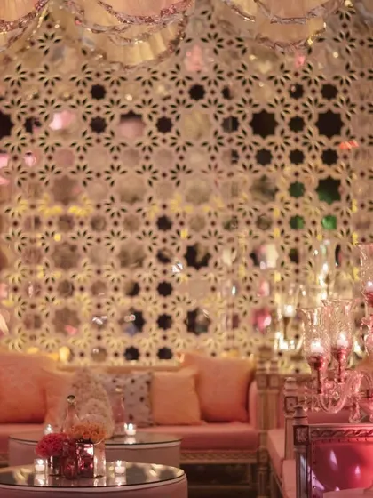 This shot showcases the comfortable and stylish lounge seating within the Sheesh Mahal setup. The soft pink sofas and mirrored tables provide a perfect space for guests to relax and socialize in a glamorous setting.