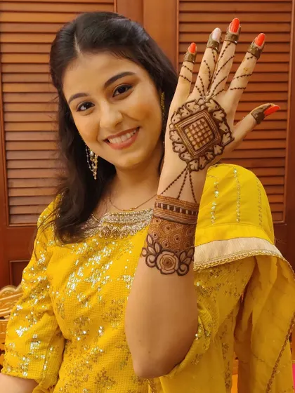 A happy client showing off her jewelry-style henna. This design features a central motif connected to the finger with delicate chains, mimicking a haath phool.