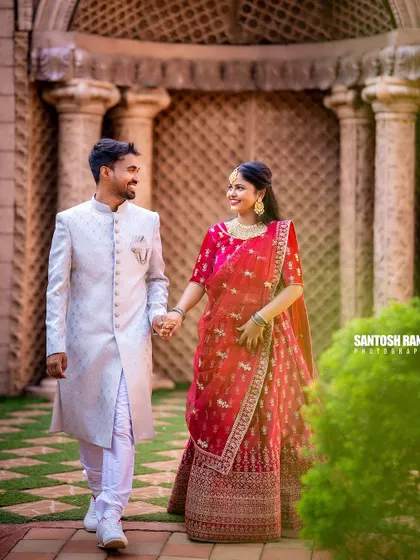 A classic walking shot of a couple in elegant traditional outfits, hand in hand through a beautiful colonnade.