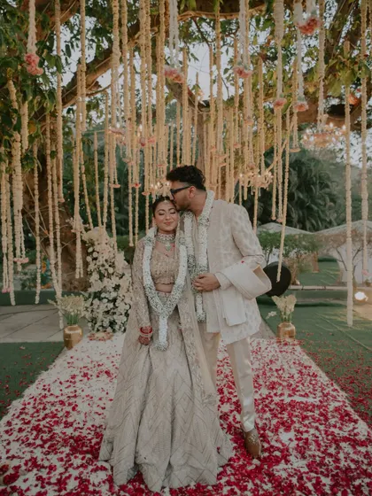 A tender moment under a tree adorned with floral hangings, as the groom kisses the bride's forehead after their Varmala.