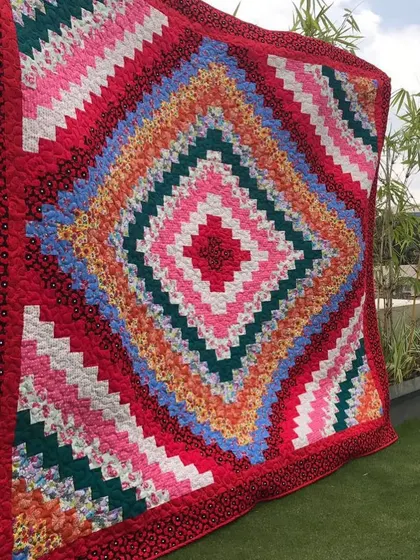 A vibrant Log Cabin quilt with a "barn raising" setting, where colors radiate from a central diamond. This piece is displayed outdoors, showing its impressive scale.