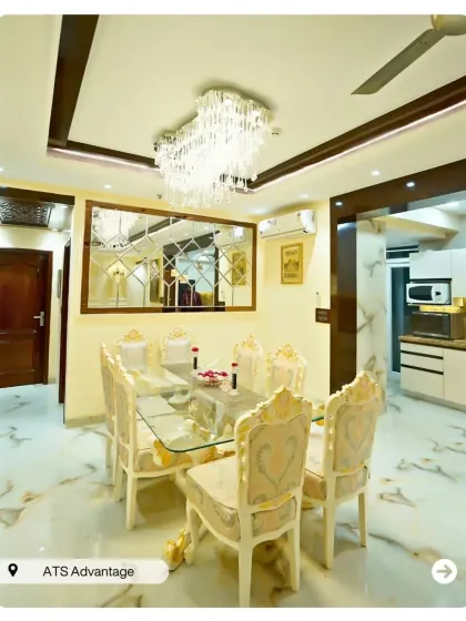 A luxurious dining room with a glass-top table and ornate, gold-accented chairs. The large mirrored wall panel makes the space feel larger and more opulent.