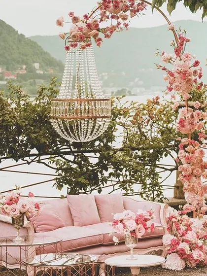 A romantic and picturesque seating area for two. The vintage pink sofa, floral arch, and hanging chandelier create a perfect photo spot, especially with a beautiful natural backdrop.