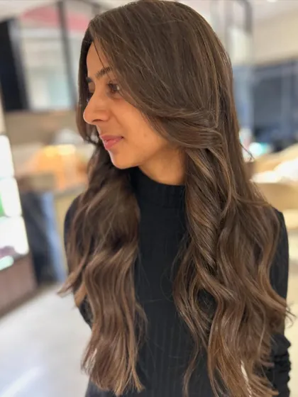 A side view of this beautiful first-time hair color. The long face-framing layers and balayage highlights create a soft and flattering look.