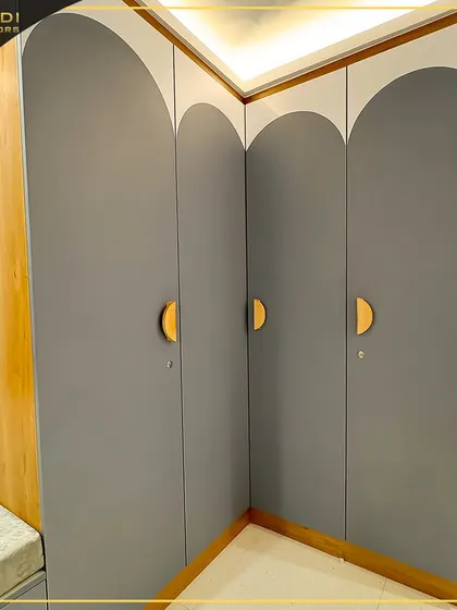 A unique corner wardrobe solution with curved grey doors and semi-circular wooden handles. This design cleverly utilizes corner space while adding a soft, modern touch.