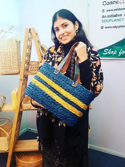 A customer showcasing our striped blue and yellow tote bag, made from woven natural fibers with durable leather-style straps. This spacious and stylish bag is perfect for work, shopping, or as a chic everyday carryall.