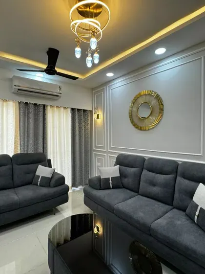 A living room designed for comfort and style, featuring dark grey sofas, elegant wall molding, and a modern chandelier, creating a sophisticated space for relaxation.