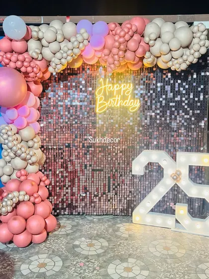 A full view of the 25th birthday backdrop, showcasing the interplay between the shimmer wall, neon sign, and marquee numbers. The organic balloon garland adds texture and dimension.