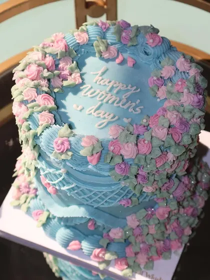 A stunning vintage-style cake for Women's Day. The beautiful blue frosting is adorned with a cascade of delicate pink and purple buttercream flowers, celebrating the grace and strength of women.