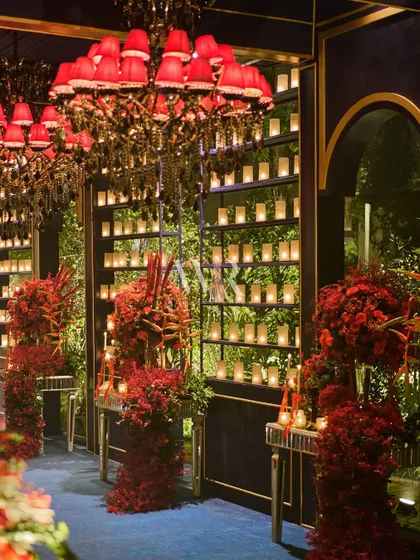 The candle wall and floral-lined entrance, with the striking red chandelier, creates a sense of drama and anticipation.