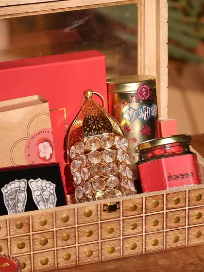A close-up of the red-themed wooden box hamper, showing the crystal lantern and silver Lakshmi feet in detail.