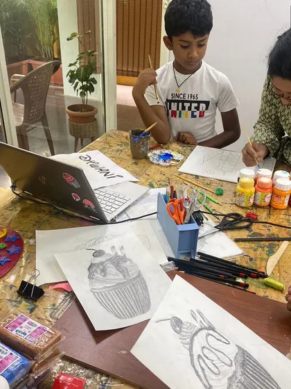 I'm helping a student with his cupcake sketch, while another works on a laptop. We blend traditional and modern tools in our classes.