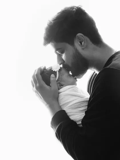 A father's love is gentle and strong. This backlit black and white portrait of a dad kissing his newborn's forehead is full of emotion.