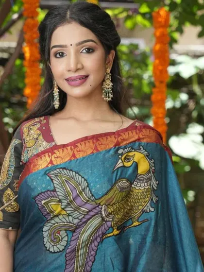 A model showcases a hand-painted Kalamkari saree with a large peacock motif, paired with oversized traditional earrings.