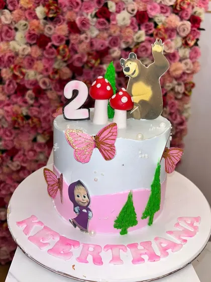 A cute 'Masha and the Bear' themed cake, perfect for a second birthday. It includes character toppers and little fondant mushrooms to create a forest scene.