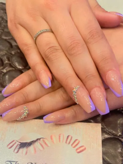A modern take on the French manicure with lavender tips on a nude, coffin-shaped base. The ring fingers are accented with a delicate trail of crystals for an elegant touch.