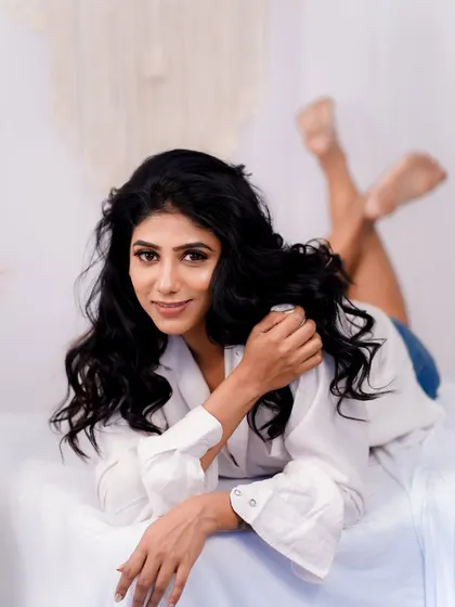 A full-body shot from a relaxed indoor session. The clean, fresh makeup complements the simple white shirt and denim shorts for a timeless and casual look.