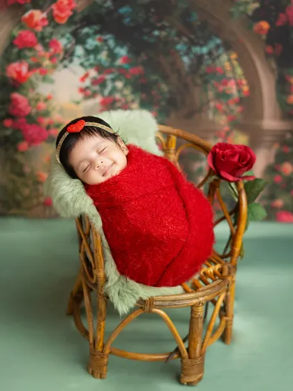 A sleeping beauty in a garden of roses. This newborn girl, wrapped in a vibrant red, looks so serene in this romantic and floral-themed setup.
